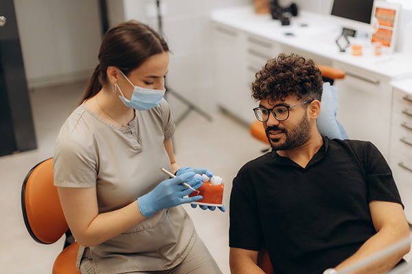 Dentist explaining full-arch implant treatment options to a patient using a dental model during a consultation