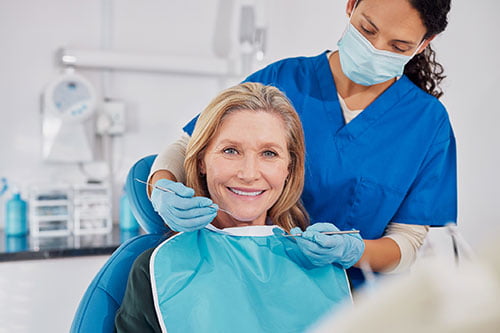 Smiling older woman at a dental clinic demonstrating the importance of proper care and maintenance for a dental bridge.