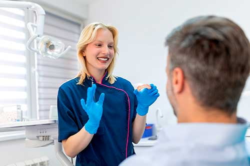 Dentist showing a dental model to a patient while explaining the lifespan and care of a dental bridge.