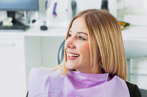 Young woman smiling during a dental appointment while learning about options for replacing a missing tooth.