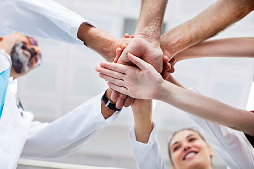 Dental team stacking their hands together to represent shared standards and collaboration across local clinics