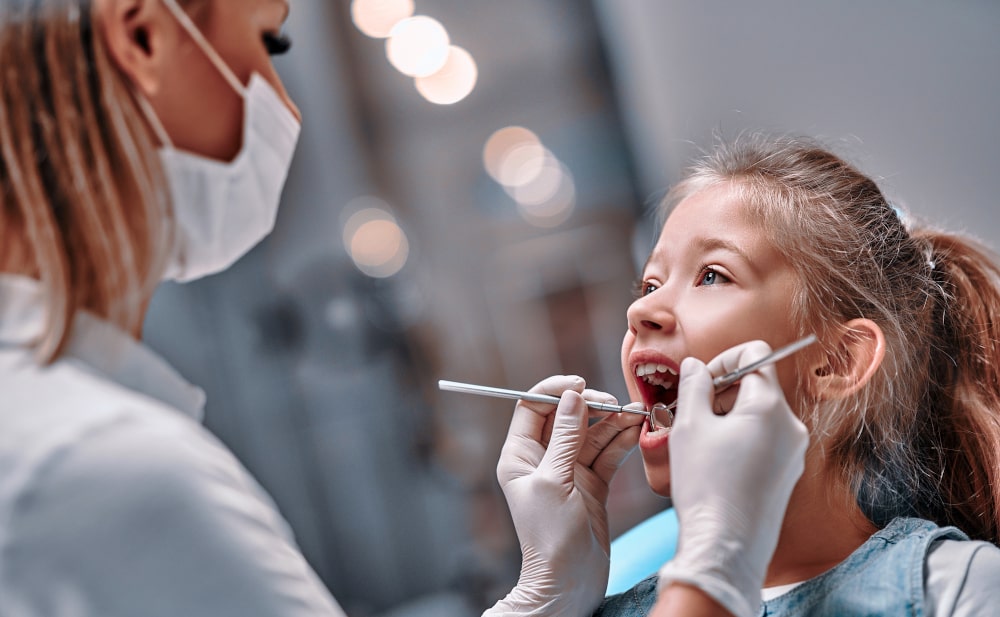 Pediatric dentist examining child’s teeth for signs of bruxism Child receiving dental check-up to monitor and assess signs of childhood bruxism