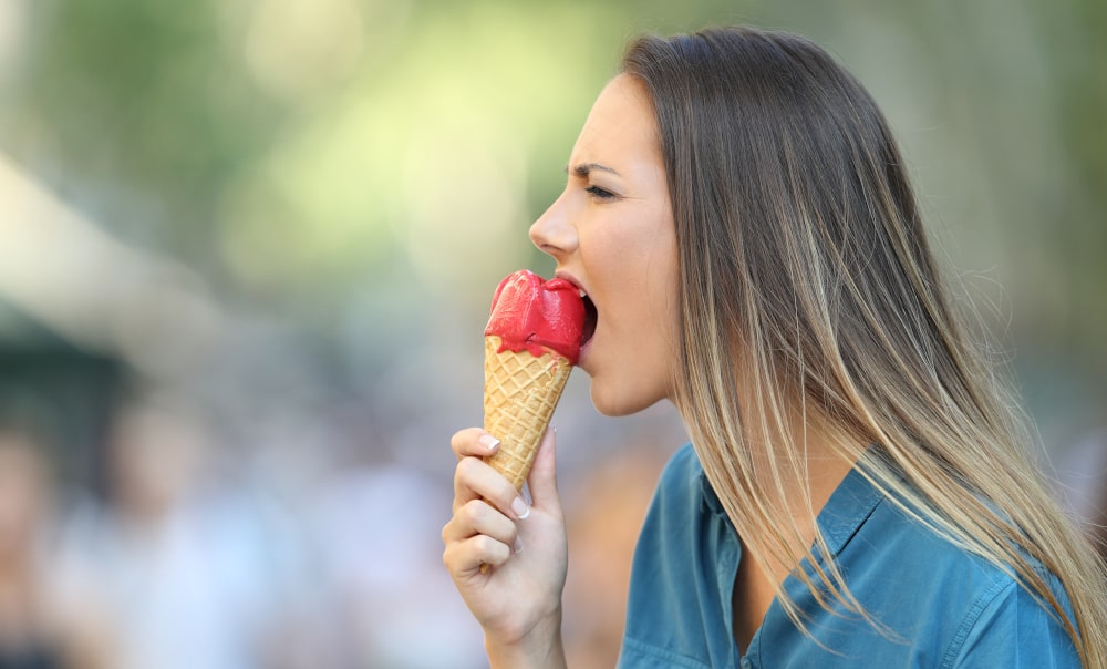 Woman feeling sharp pain in her teeth after eating ice cream due to cold sensitivity