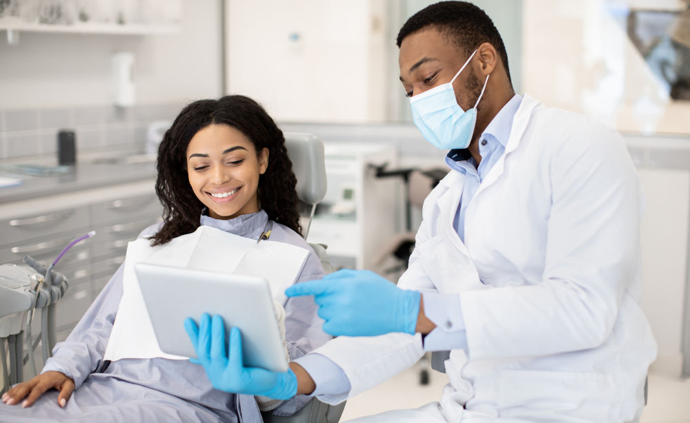 Dentist reviewing information on a digital tablet with a patient, representing discussion of experience, procedure options, and case-specific planning during a cosmetic dentist consultation.