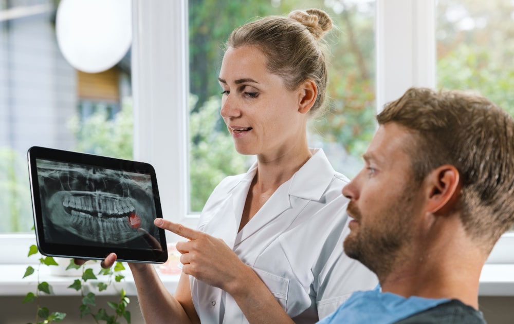 Female dentist discussing dental X-ray results of wisdom teeth with male patient