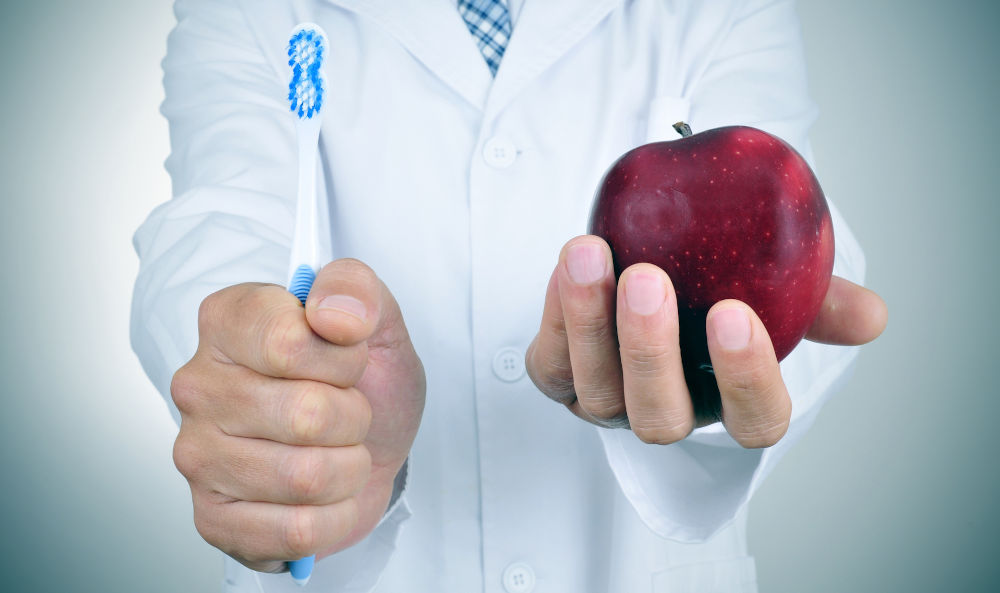 Dentist showing a toothbrush and an apple, illustrating the importance of brushing after meals to prevent plaque buildup and gingivitis.