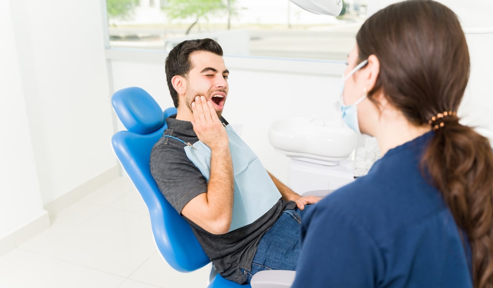 Latin man grimacing in pain during a dental visit due to an infected wisdom tooth